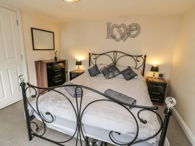 A bedroom with a black metal bed frame a dresser two bedside tables with lamps and a wall decoration spelling love at Cairns Cottage in Whitby