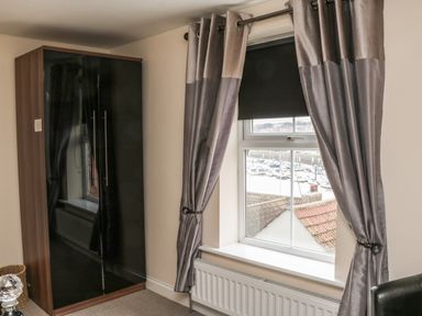 A bedroom corner with a wardrobe curtains and a window overlooking boats at Cairns Cottage in Whitby