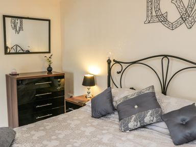 A bedroom with a bed with pillows bedside table with lamp and a chest of drawers with a mirror above at Cairns Cottage in Whitby
