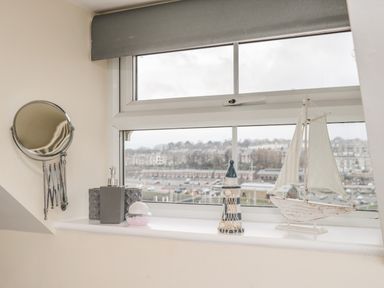 A window with decorative items including a wall-mounted mirror, soap dispenser, small bowl, lighthouse figurine, and sailboat model at Cairns Cottage in Whitby