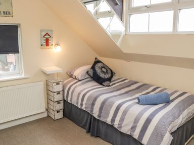 A bedroom with a single bed under a sloped ceiling with a striped bedspread and a blue towel at Cairns Cottage in Whitby