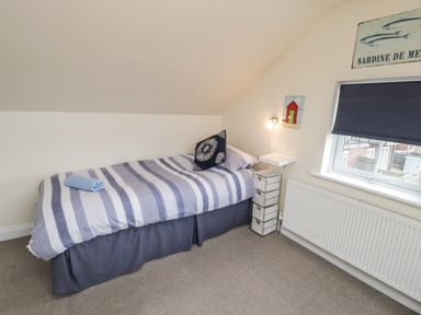 A bedroom with a striped bed and wicker drawers under a sloped ceiling at Cairns Cottage Whitby