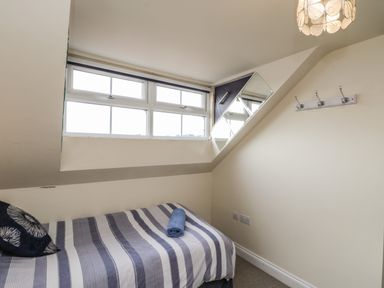 A small bedroom with a single bed under a window and a mirror on the wall at Cairns Cottage in Whitby
