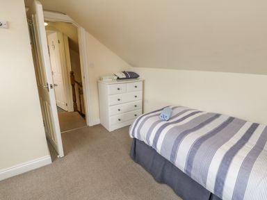 A bedroom with a single bed, chest of drawers, an open door, and a sloped ceiling at Cairns Cottage in Whitby