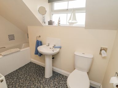 A bathroom with a bathtub sink toilet blue towels window and nautical decorations at Cairns Cottage in Whitby