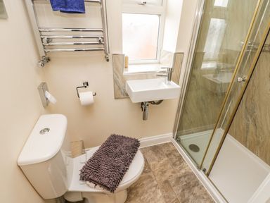 A bathroom with a toilet a small sink a shower enclosure and a towel rack at Cairns Cottage in Whitby