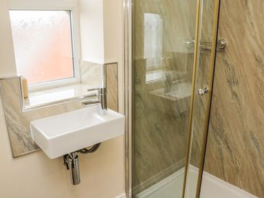 A bathroom with a rectangular white sink and a chrome faucet next to a glass shower enclosure with marble patterned walls at Cairns Cottage in Whitby