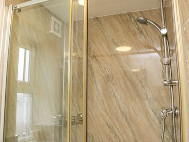A shower with glass doors and a wall-mounted showerhead in a bathroom at Cairns Cottage in Whitby