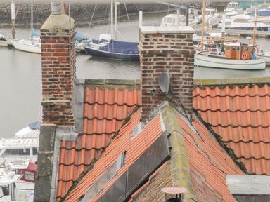 A view of red tiled rooftops with brick chimneys and boats docked on water in the background at Cairns Cottage in Whitby