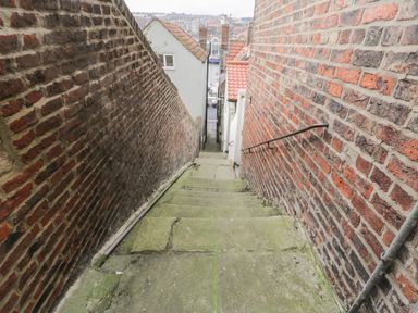 A narrow stone staircase descending between two brick walls in an outdoor urban area at Cairns Cottage in Whitby