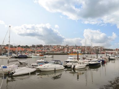 A marina with several boats docked on calm water and buildings in the background at Cairns Cottage in Whitby