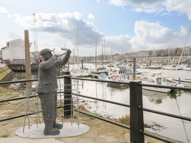 A wire sculpture of a man playing golf near a marina with boats and buildings in the background at Cairns Cottage in Whitby