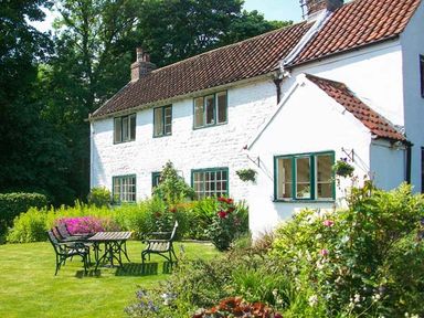 A garden with metal table and chairs in front of a white house with a tiled roof at The White Cottage in Bridlington