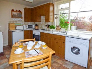 A kitchen with wooden cabinets a dining table set with cups plates and orange juice at The White Cottage in Bridlington