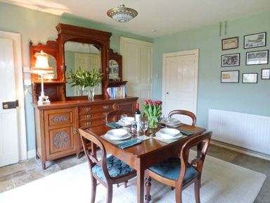 A dining room with a wooden table set for four and a wooden sideboard with a mirror at The White Cottage in Bridlington