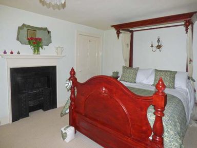 A bedroom with a wooden four poster bed a fireplace and a mirror above the mantel at The White Cottage in Bridlington