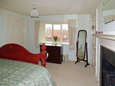 A bedroom with a wooden bed a chest of drawers a standing mirror and a fireplace at The White Cottage in Bridlington
