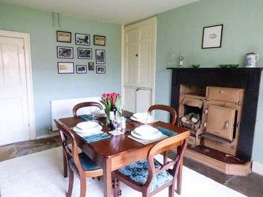 A dining room with a wooden table set for four near a fireplace and wall pictures at The White Cottage in Bridlington