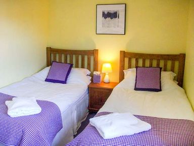 A bedroom with two single beds a wooden nightstand lamp and framed artwork at The White Cottage in Bridlington
