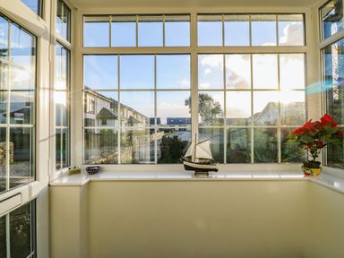 A porch area with large windows a model sailboat and a potted plant at Ty'r Ysgol in Morfa Bychan