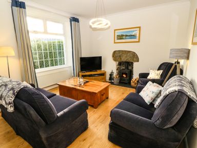 A living room with two dark sofas a wooden coffee table a television a fireplace and large window at Ty'r Ysgol in Morfa Bychan