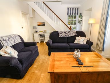 A living room with two navy sofas a wooden coffee table a desk under stairs and a window with striped blinds at Ty'r Ysgol in Morfa Bychan