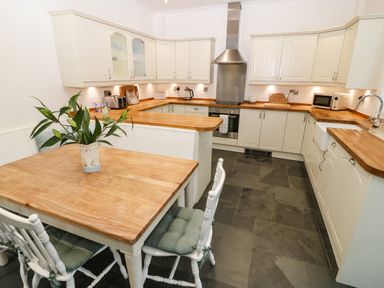 A kitchen with wooden countertops white cabinets a dining table with chairs and a plant on the table at Ty'r Ysgol in Morfa Bychan