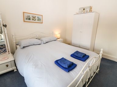 A bedroom with a double bed with blue bedding two folded blue towels a white wardrobe and bedside tables at Ty'r Ysgol in Morfa Bychan