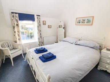A bedroom with a bed with folded towels a wicker chair and a window with curtains at Tyr Ysgol in Morfa Bychan