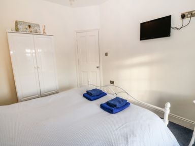A bedroom with a white bed frame and folded blue towels on the bed next to a white wardrobe and a wall-mounted TV at Ty'r Ysgol in Morfa Bychan