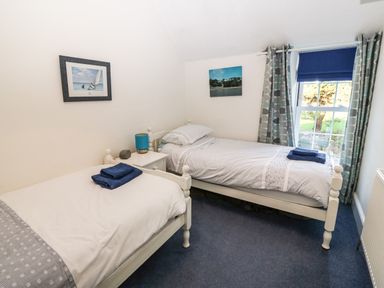 A bedroom with two single beds bedside table with lamp window with curtains and blinds at Ty'r Ysgol in Morfa Bychan