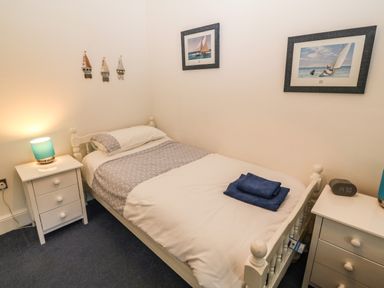 A bedroom with a single bed flanked by two bedside tables each with a lamp and wall art of sailboats at Ty'r Ysgol in Morfa Bychan