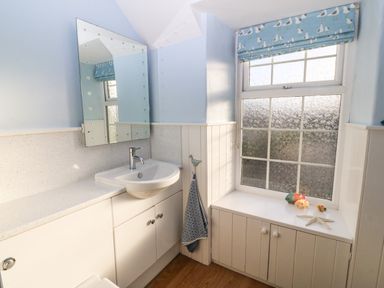 A bathroom with a sink under a mirror and a window with decorative blinds at Ty'r Ysgol in Morfa Bychan