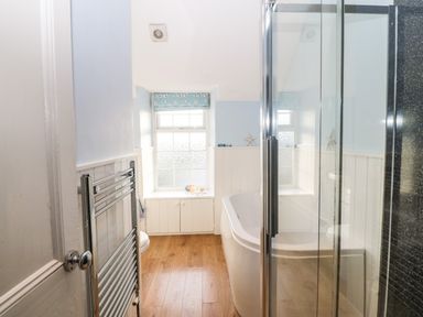 A bathroom with a bathtub next to a window a glass shower enclosure a heated towel rail and wooden floor at Ty'r Ysgol in Morfa Bychan