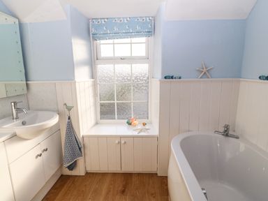 A bathroom with a sink, bathtub, window with a blue seagull-patterned blind and wooden floor at Ty'r Ysgol in Morfa Bychan