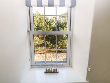 A window with a striped blind and small decorative beach huts on the sill at Ty'r Ysgol in Morfa Bychan