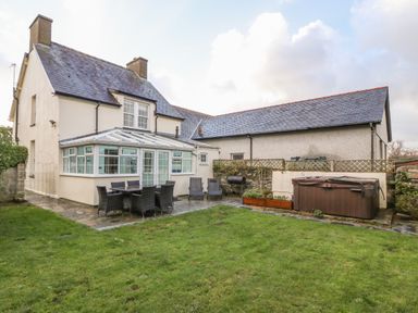 A backyard with a patio dining set barbecue grill hot tub and a house with conservatory at Tyr Ysgol in Morfa Bychan