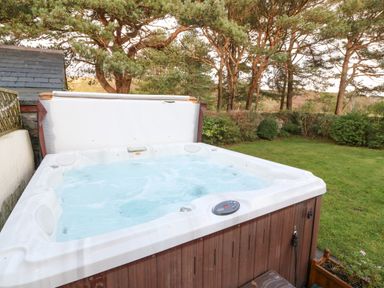 An outdoor hot tub with bubbling water in a garden surrounded by trees and shrubs at Ty'r Ysgol in Morfa Bychan