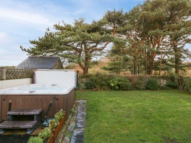 An outdoor garden area with a hot tub on the left and trees and bushes in the background at Ty'r Ysgol in Morfa Bychan