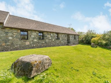 A stone cottage with three windows and grass lawn with large rocks at Foxglove in Newport Pembrokeshire