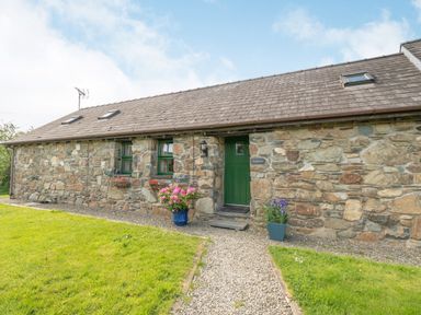 A stone exterior building with green door and windows with flower pots on a gravel path at Foxglove in Newport Pembrokeshire