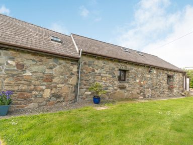 A stone exterior wall of a house with small windows and a sloped roof with skylights at Foxglove in Newport Pembrokeshire