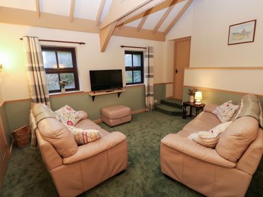 A living room with two beige sofas a wall-mounted TV and green carpet at Foxglove in Newport Pembrokeshire