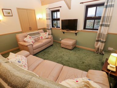 A living room with beige sofas a television on a wall shelf and striped curtains at Foxglove in Newport Pembrokeshire