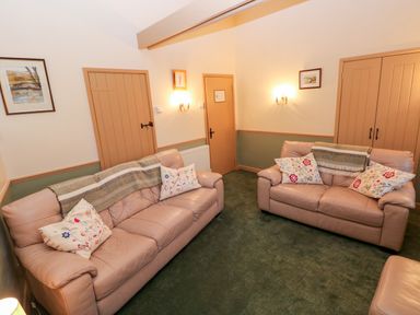 A living room with two beige sofas with pillows and blankets green carpet and three peach colored doors at Foxglove in Newport Pembrokeshire