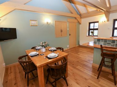 A dining area with a wooden table set for four and a bar counter with stools at Foxglove in Newport Pembrokeshire