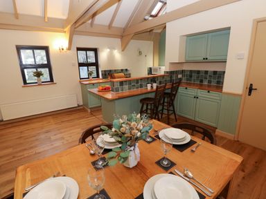 A dining area with a set table and a kitchen with cabinets and bar stools at Foxglove in Newport Pembrokeshire