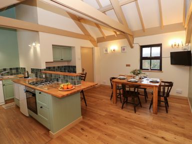 A kitchen and dining area with wooden beams wooden floor a dining table with chairs and a kitchen island with a stove at Foxglove in Newport Pembrokeshire