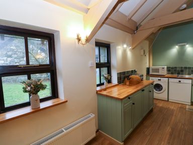 A kitchen with wooden countertops green cabinets a washing machine dishwasher microwave and two windows with flowers on the sills at Foxglove in Newport Pembrokeshire