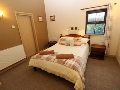 A bedroom with a double bed between two wooden bedside tables and a window with curtains at Foxglove Newport Pembrokeshire